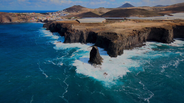 Dramatic coastal landscape, rugged volcanic cliffs meeting the deep blue Atlantic Ocean. Powerful ocean waves crashing against a solitary sea stack