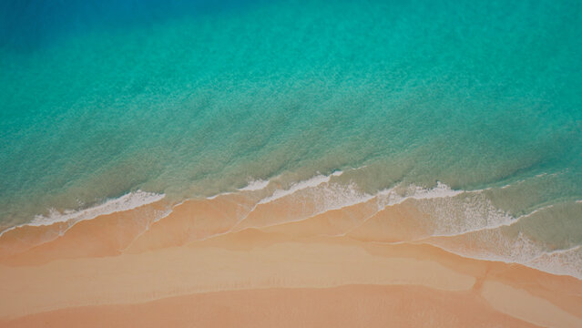 Aerial view of a pristine tropical beach, turquoise ocean waves gently lapping against soft golden sand, a serene coastal landscape for travel and vacation themes.