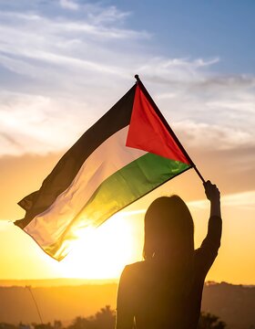 Woman waving Palestinian flag at sunset.