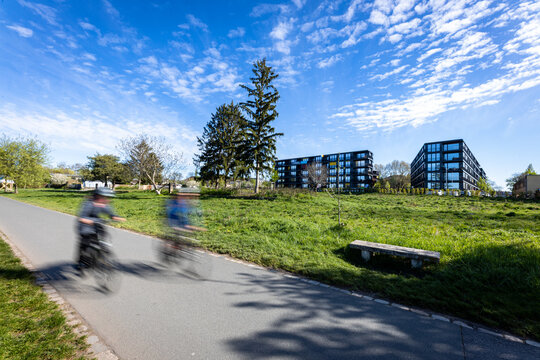 Cyclists riding along the Elbe Cycle Path (Elberadweg) in Dresden, Germany, on a sunny day. Motion blur highlights the speed of cyclists on a paved riverside bike path, surrounded by green grass and t