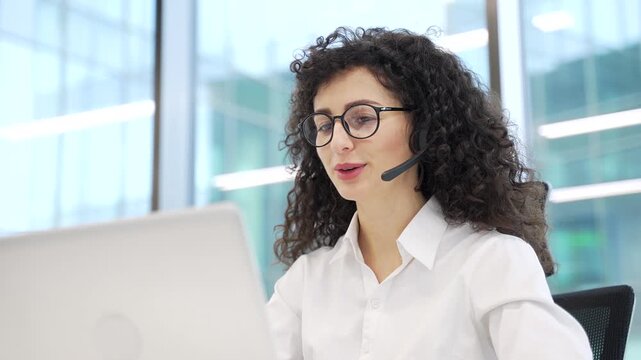 Female corporate operator in headset working in customer support service on helpline telesale talking using laptop sitting at workplace in business office. Agent of call center advises client Close up