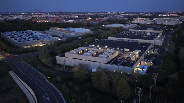 Aerial dusk view of illuminated data center campus in Ashburn Virginia, with roads, passing cars and modern server facilities under blue hour sky in United States technology corridor. Wide shot.
