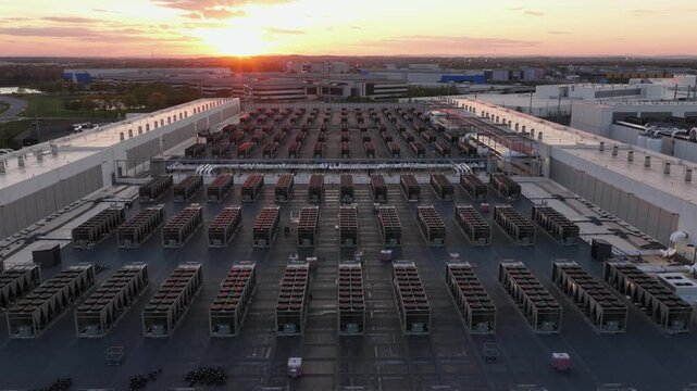 Aerial drone flyover of modern data center campus in Ashburn, Virginia, USA at sunset, showing rooftop cooling systems, technology infrastructure and expansive server facility complex.