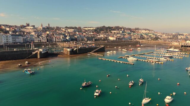 St Peter Port Harbour Guernsey.Forward golden hour footage over the outer harbour to Victoria Marina entrance and visitor pontoons and boats on swinging moorings with clear blue calm water at low tide