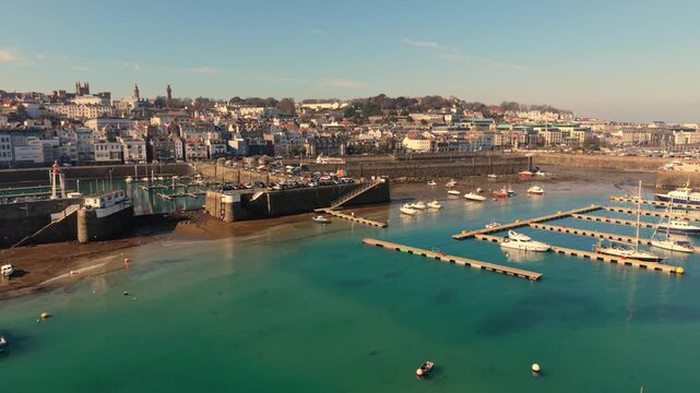 St Peter Port Harbour Guernsey.Forward golden hour footage over the harbour to Victoria Marina entrance and visitor pontoons and boats drying out with clear blue calm water at low tide