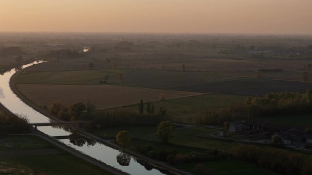 Patchwork of agricultural fields rotates into view with canal edge and tree lines defining land use across extensive flat plain under warm low light, lateral yaw movement