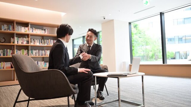 綺麗な会社の社長室で商談後に握手するビジネス契約成功と協業や成立の動画　経営者と営業のイメージ広角の全身