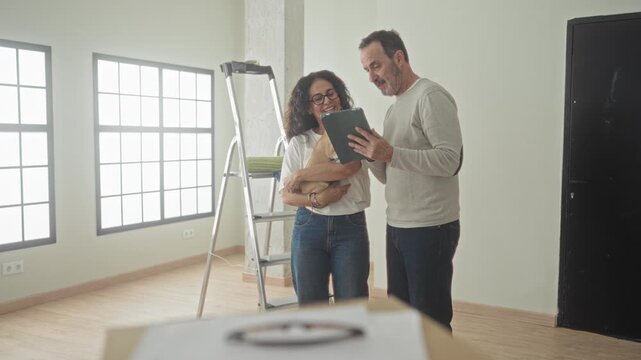 Man holding tablet while woman points and cradles dog in empty apartment building; renovation planning hopeful.