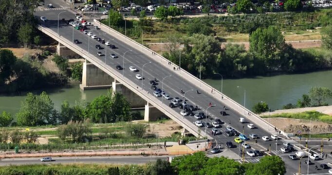Aerial view of the Marconi Bridge in Rome, Italy, showing traffic crossing the Tiber River. The scene captures the urban infrastructure and green riverbanks of the Italian capital from above.