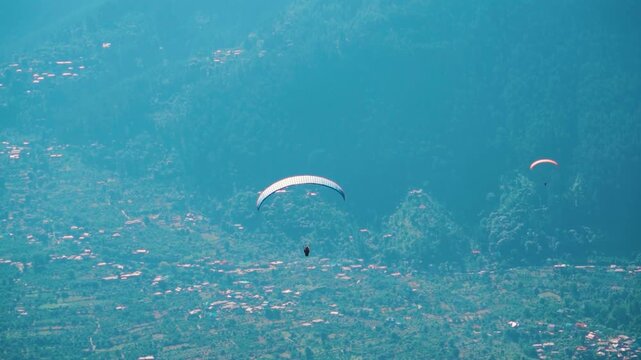 Paraglider flying against a beautiful mountain valley in Dobhi at Manali, Himachal Pradesh, India. Tourist flies with parachute. Adventure activity in Manali.