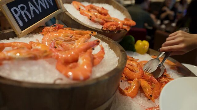 Person Using Tongs to Pick Fresh Prawns from Ice Buffet