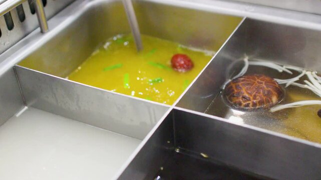 Ladle Serving Hot Mushroom Broth in a Divided Chinese Hot Pot