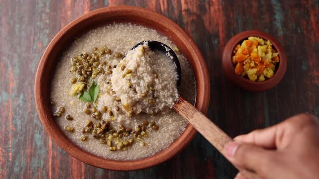 Millet porridge in a mud plate on a wooden table. Millet porridge with lentils healthy breakfast or dinner. Diabetes friendly meal. Kanji fox tail millet in Kerala India.
