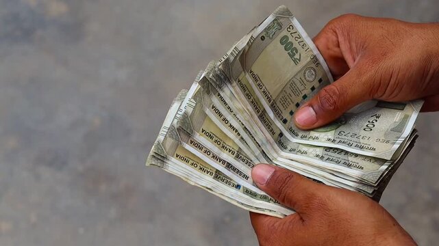 Close up of an Indian man counting five hundred rupee notes outdoors, male hands holding and counting Indian currency cash, finance and investment concept

