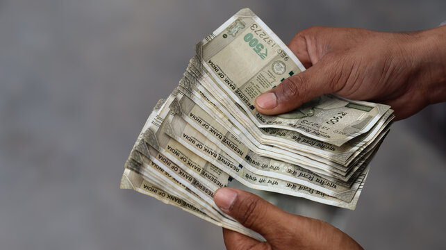 Close up of male hands holding a stack of Indian five hundred rupee notes, hands counting cash currency, business finance and investment concept
