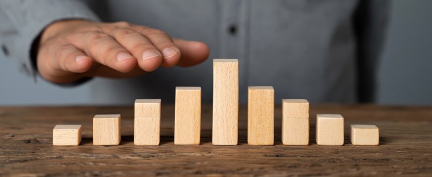 Entrepreneur's hand halting toppling wooden cubes to avoid cascade effect, representing risk management, leadership, and strategic planning in business environment.