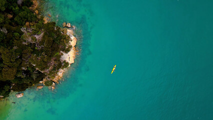 Aerial view of a vibrant turquoise ocean with a lone yellow kayak, serene coastal waters next to a lush green island, tranquil summer seascape for travel and nature themes © Kuch_Bhi