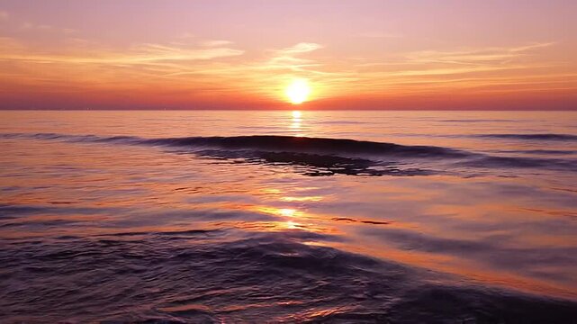 Sunset over the ocean with vibrant orange and pink hues reflecting on gentle waves and foamy shoreline