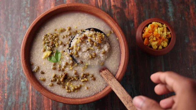 Millet porridge in a mud plate on a wooden table. Millet porridge with lentils healthy breakfast or dinner. Diabetes friendly meal. Kanji fox tail millet in Kerala India.
