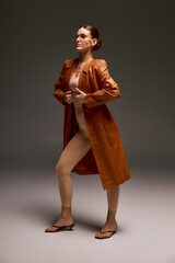 Fototapeta premium Stylish young woman in a leather coat showcasing modern fashion in a studio setting