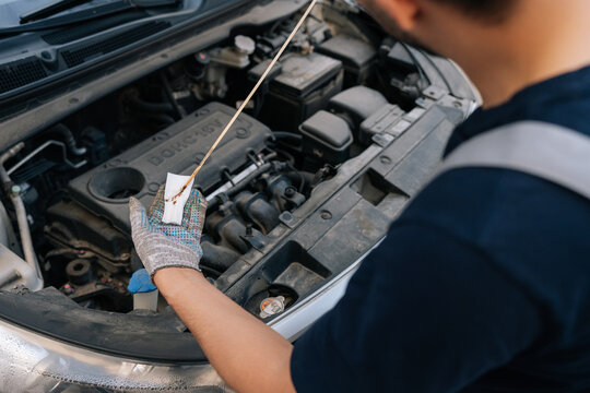 Auto mechanic performing essential car maintenance, checking engine oil level with dipstick and wiping it clean, ensuring proper vehicle function and performance.