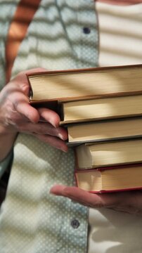 Female student holding stack of textbooks in hands close-up, vertical video
