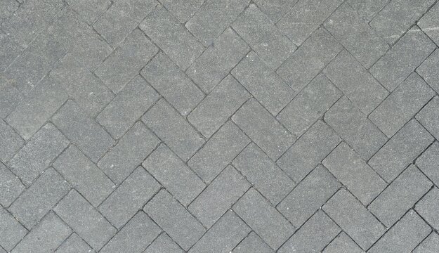 Grey herringbone pattern paving blocks. Grey concrete paving blocks in a seamless herringbone pattern. Gritty stone pavement texture featuring high-quality aggregate details.