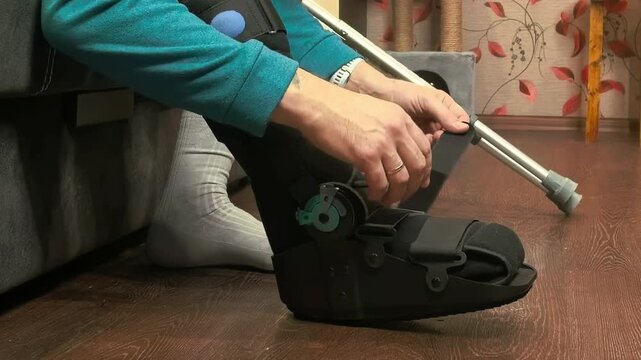 Close up hands fastening orthopedic boot buckles indoors, injury recovery process, rehabilitation and medical support concept.