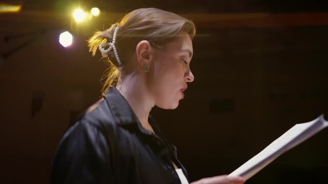 Focused stage rehearsal with actors reading scripts under theatrical lighting, capturing concentrated expressions, performance preparation, and dramatic atmosphere