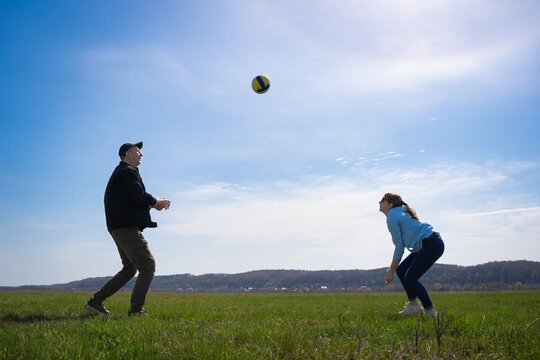 Two adults playing volleyball on a sunny day in an open grassy field, passing the ball and enjoying active fitness, fresh air, teamwork and leisure under a clear blue sky