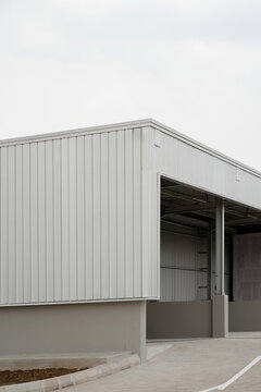 Corner exterior view of modern industrial warehouse building with corrugated metal siding, open entrance bay, and concrete driveway.