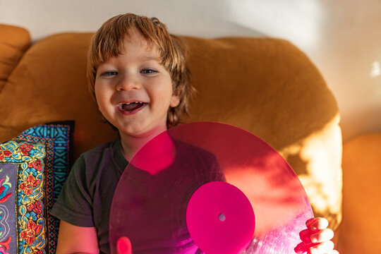 Smiling child playing with pink vinyl record indoors