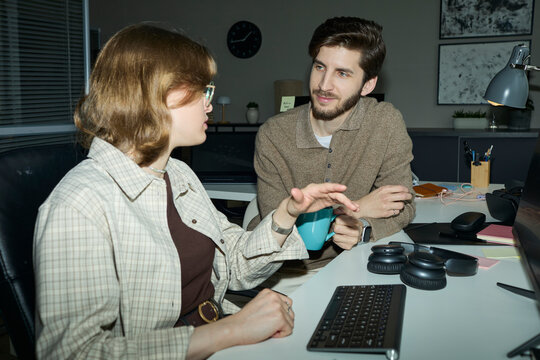 Programmer colleagues discuss work at the office desk at night