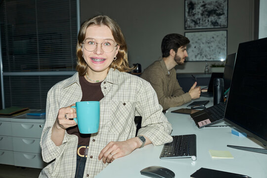 Smiling woman programmer having coffee break at office desk