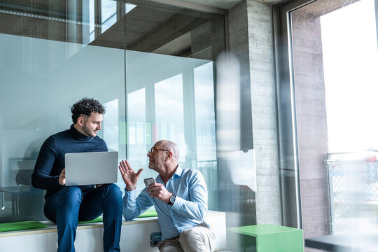 Businessman and colleague discussing work with laptop in office