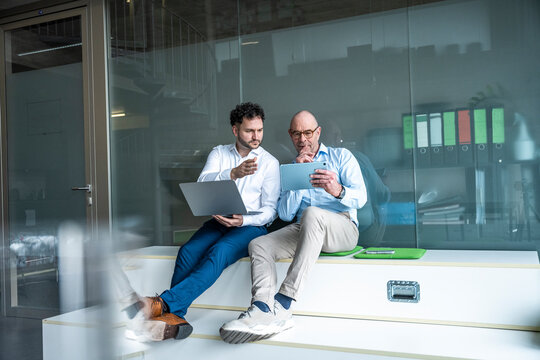 Coworkers discussing work with tablet and laptop in modern office