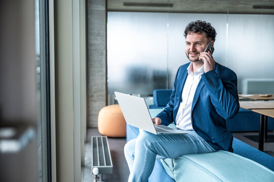 Smiling businessman working on laptop and calling in office
