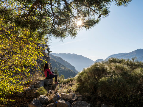 Outdoor lifestyle travel: Woman hiker relaxing on rocks, enjoying a sunny mountain view amidst nature at Forra del Lupo Trekking, Trentino, Italy.