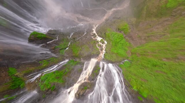 Cinematic FPV drone dive over the stunning multi-stream Tumpak Sewu waterfall, surrounded by lush rainforest cliffs in East Java, Indonesia.