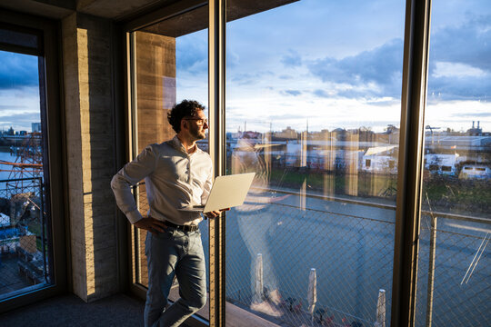 Businessman standing by office window with notebook in the evening