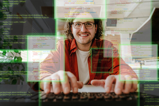 Smiling programmer typing code with digital hologram at office