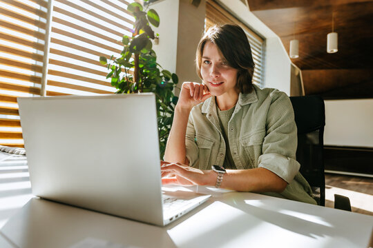 Businesswoman working on laptop at modern office desk in sunlight