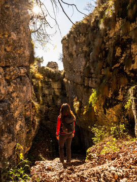 Trekking woman with backpack exploring a sunlit rocky gorge with autumn foliage, embodying outdoor adventure and travel lifestyle in Forra del Lupo Trekking, Trentino, Italy.