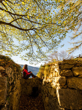 Woman hiker exploring historical World War I trenches in autumn, Forra del Lupo Trekking, Trentino, Italy, offering a travel and adventure lifestyle.