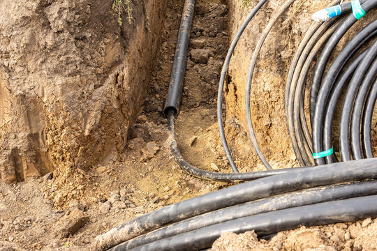Thick walled plastic protective pipe and armored cables in excavation trench for underground utility installation under roadway