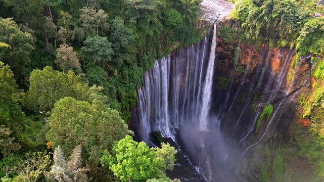 Aerial drone view of Tumpak Sewu waterfall in East Java, Indonesia. Spectacular curtain waterfall surrounded by dense tropical jungle and cliffs, showcasing powerful cascading water and natural beauty