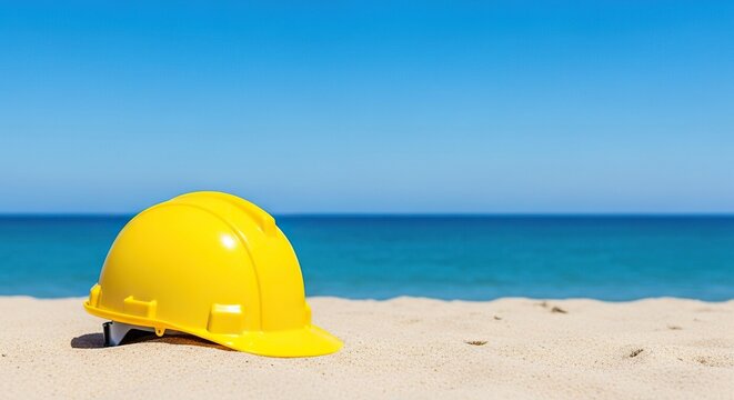 A bright yellow hard hat sits on a soft sandy beach, framed by the deep blue ocean and a cloudless sky, blending industry and relaxation, summer, vacation, seaside