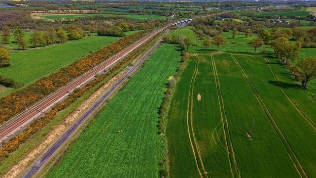 High-speed train railway line and viaduct cutting through green fields in rural Mayenne, France. Aerial forward