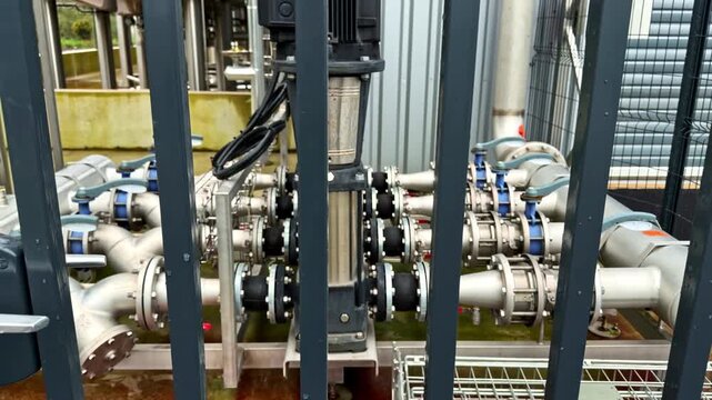 A detailed view of interconnected pipes and valves, secured behind metal bars. Ideal for industrial infrastructure or engineering content.
