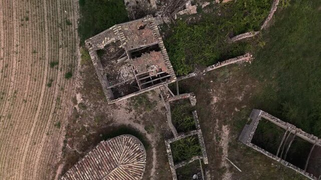 Aerial drone view of abandoned stone ruins of Capella de Santa Fe de Montfred surrounded by agricultural fields and vegetation. Top down view of historic rural chapel remains 